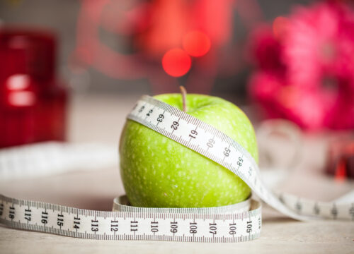 Photo of a green apple covered in measuring tape next to red Christmas decorations